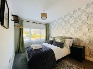 Een verzorgde slaapkamer met een bed, nachtkastjes, een hanglamp en een raam met gordijnen.