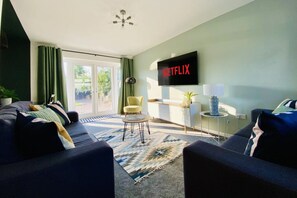 Ein modernes Wohnzimmer mit einer Couch, einem Sessel und einem Couchtisch. Ein Flachbildfernseher an der Wand zeigt das Netflix-Logo.
