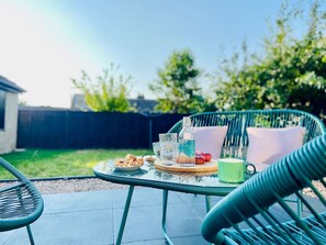 Un patio con una mesa dispuesta para una comida, que incluye un plato de comida, un vaso de agua y una botella.