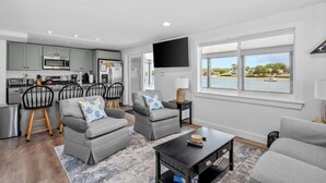 A modern living room with grey sofas, a black coffee table, and a view of a lake.