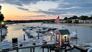 A marina with docked boats, a small wooden building with an American flag, and a calm water body reflecting the sky.