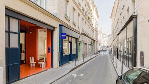 Une rue étroite, avec un hôtel-boutique situé sur le côté gauche, qui se distingue par son design moderne et sa façade rouge et bleue.