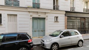 Une vue de rue avec deux voitures garées, un immeuble avec une porte verte et une clôture en fer forgé.