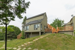 A two-story building with a staircase leading to a deck, surrounded by greenery.