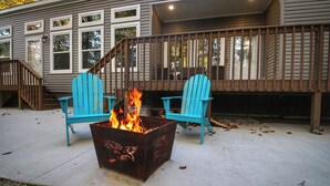 Una terraza con dos sillas Adirondack azules y un brasero metálico con llamas.