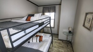 Habitación con literas, una ventana, una mesita con una vela y un cuadro en la pared.