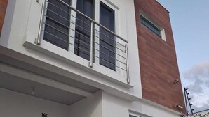 A two-story building with a white facade, a balcony with metal railings, and a garage door marked with the number 16C.