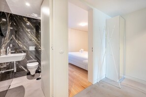 Enjoy a spacious bedroom with a comfortable white bed and a large mirror, adjacent to a modern bathroom with a sink and bathtub.