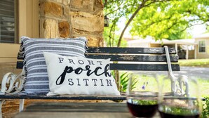 Un banc avec un coussin sur lequel est inscrit « Pour se détendre sur le porche » et deux verres de vin rouge.