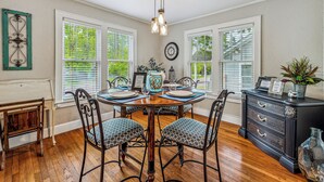 Un coin repas comprenant une table en bois, quatre chaises, un meuble noir et un luminaire suspendu.