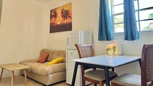 Un espace de vie compact comprenant un canapé, une petite table, un réfrigérateur et une fenêtre avec des rideaux.