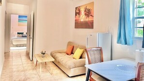 Un espace de vie compact comprenant un ventilateur de plafond, un canapé avec des coussins, une petite table et une fenêtre avec des rideaux.