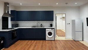 A modern kitchen with dark blue cabinets, a built-in washing machine, a microwave, and a stove. - Cosy Flat with Garden London (Bexleyheath)