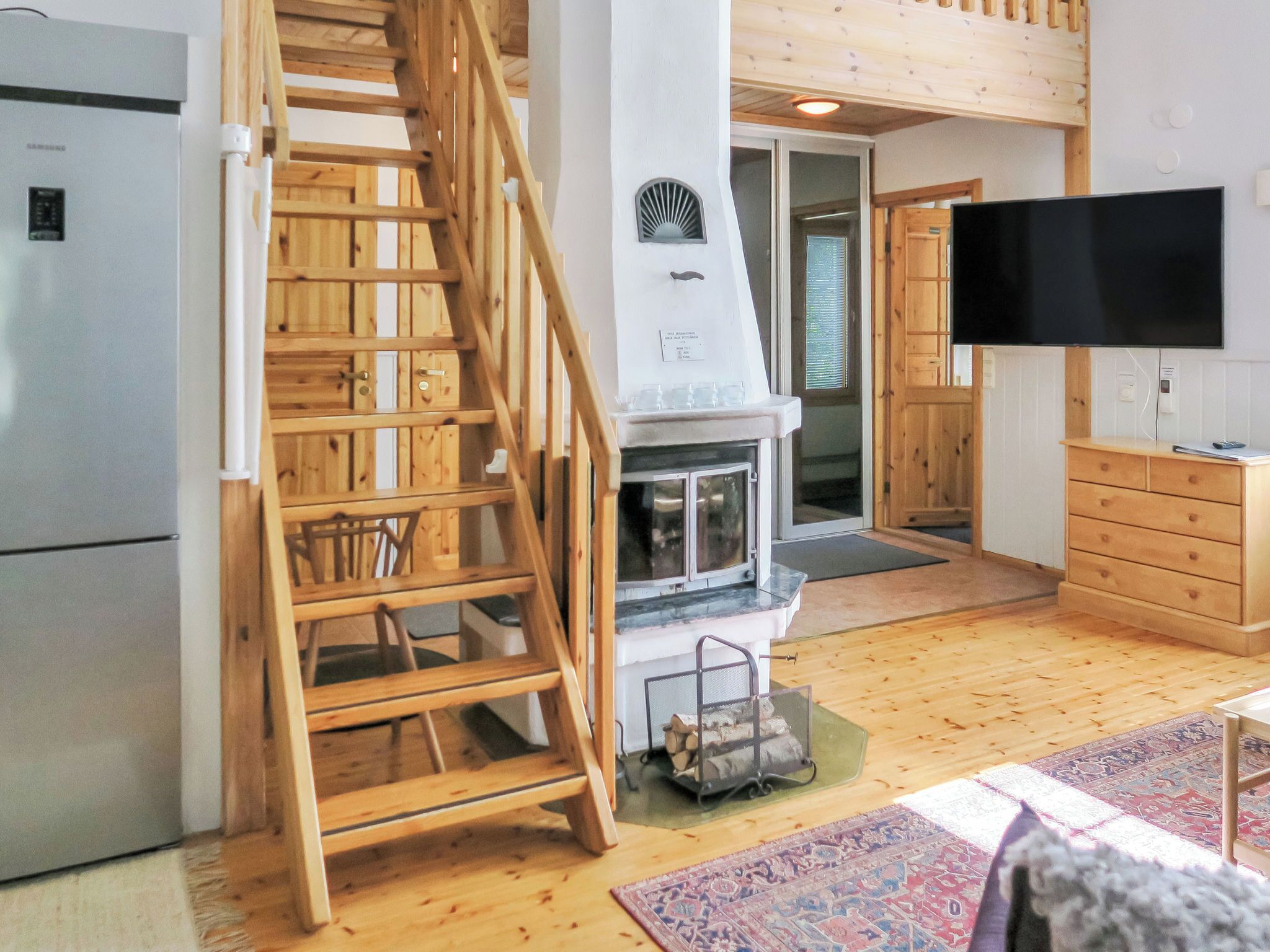 A wooden interior with a staircase, a fireplace, a television, and a refrigerator.