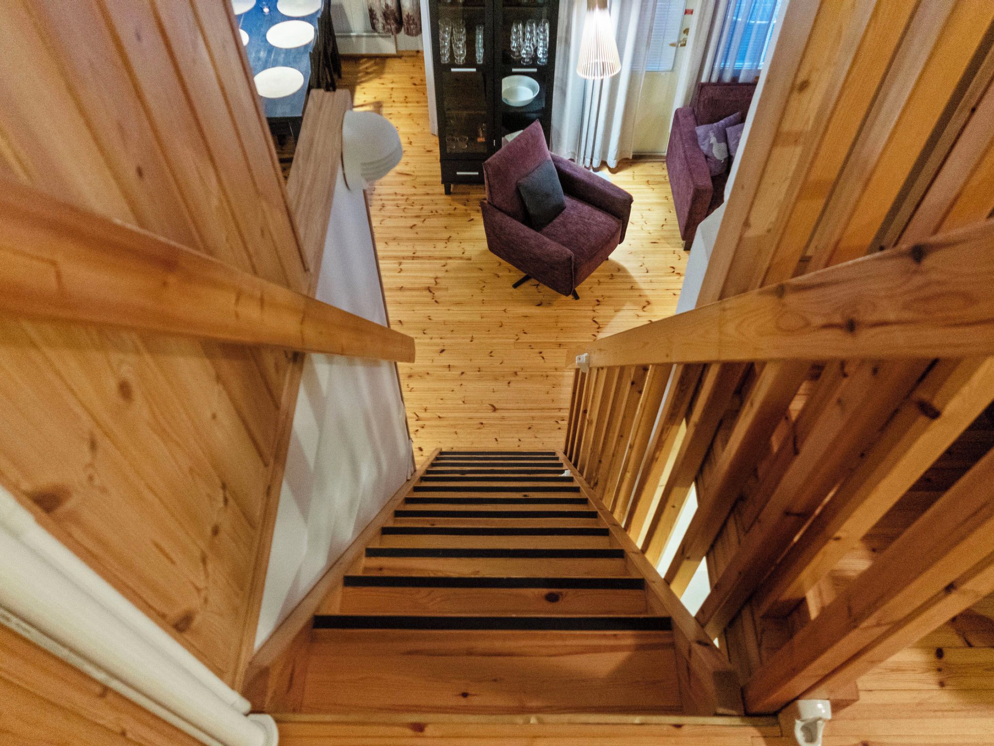 Eine Holztreppe führt zu einem Raum mit einem violetten Sofa und einem Essbereich mit einem Schrank und Stühlen.