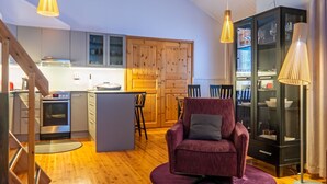 A modern kitchen with wooden cabinets, a dining area with a purple armchair, and a black cabinet with glass doors. - Katinkulma 2 by Interhome (Sotkamo)