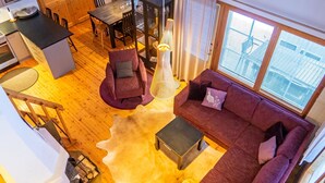 A spacious living area with a wooden floor, a purple sofa, a dining table, and a kitchen area with wooden cabinets and a black countertop. - Katinkulma 2 by Interhome (Sotkamo)