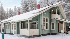 A two-story house with a green exterior and white trim, surrounded by snow-covered trees. - Katinkulma 2 by Interhome (Sotkamo)