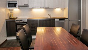 A modern kitchen with a wooden dining table, dark cabinets, and stainless steel appliances.
