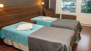 A hotel room with two single beds, a chair, a window with blinds, and a hanging light fixture.