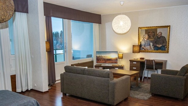 A modern living room with a sofa set, a flat-screen TV, a desk with a chair, and a painting on the wall.
