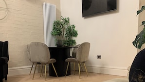 A modern living room with a beige sofa, two chairs with gold legs, a small table with a plant, and a flat-screen TV mounted on the wall. - The Nave a unique duplex apartment in a historic converted church near to beach. (Waterloo)