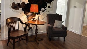 A room with a large wall-mounted animal hide, a wooden table with a lamp, a wooden chair, and a cushioned armchair. - Rodeo Ranch: Shuffleboard, Near seasonal Live Rodeo, Bunkbed, King Bed, SMOOR (Mansfield)