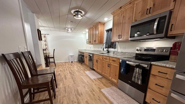 A kitchen with wooden cabinets, stainless steel appliances, and a dining area with wooden chairs. - Rodeo Ranch: Shuffleboard, Near seasonal Live Rodeo, Bunkbed, King Bed, SMOOR (Mansfield)