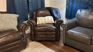 A living room with a brown leather armchair, a grey sofa, and a blue curtain. - Rodeo Ranch: Shuffleboard, Near seasonal Live Rodeo, Bunkbed, King Bed, SMOOR (Mansfield)