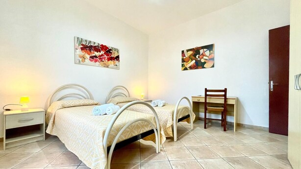 Un dormitorio con dos camas, un escritorio y una silla. Hay dos cuadros en las paredes.