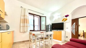 Un espacio habitable compacto con una mesa de comedor, sillas, un sofá, un televisor y una zona de cocina con armarios y un microondas.