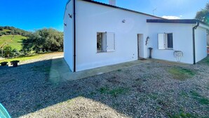 Une maison blanche d’un seul étage, avec une allée gravillonnée, une cheminée et un petit porche.