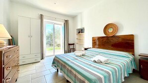 Une chambre à coucher comprenant un lit, une commode, une chaise, une bibliothèque et une grande fenêtre.