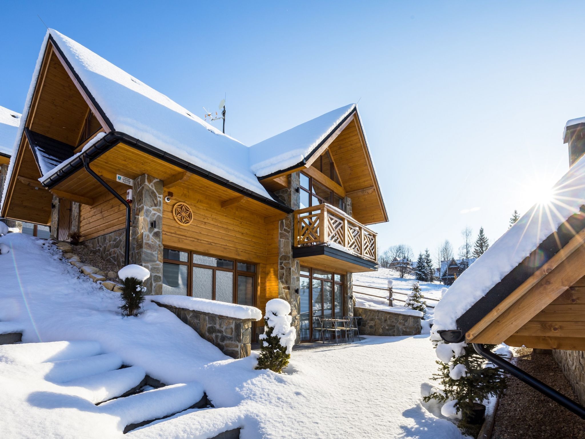 A modern log cabin with a stone foundation, wooden exterior, and a balcony with lattice railings.