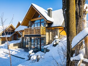 Un edificio de estilo chalet con balcón de madera y paredes de piedra, rodeado de nieve.