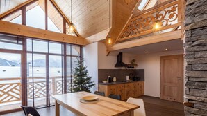 A spacious dining area with a wooden table and chairs, a kitchen with a stove and cabinets, and a large window with blinds.
