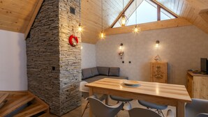 A cozy dining area with a stone wall, wooden ceiling, and a sloped roof.