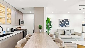 Una cocina moderna con una isla central, microondas integrado y un comedor con una mesa larga y sillas.
