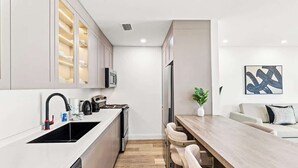 Una cocina moderna con una isla central, un comedor con taburetes de bar y una sala de estar con sofá y planta.