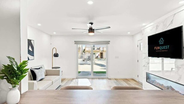 Una sala moderna con una mesa de centro de madera, un sofá con un cojín decorativo, una lámpara de pie y un televisor montado en la pared.