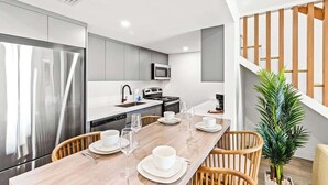 A modern kitchen with stainless steel appliances, a dining area with a wooden table and chairs, and a staircase with wooden railings.