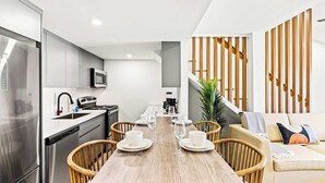 A modern kitchen with a dining area, stainless steel appliances, and a wooden dining table set for four.
