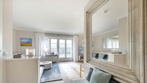 Un salon spacieux, doté d’un grand miroir, d’un canapé, d’une table basse et offrant une vue à travers les portes vitrées.