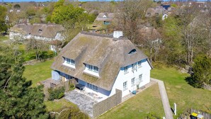 Une maison blanche avec un toit de chaume, entourée d’arbres et d’autres maisons.