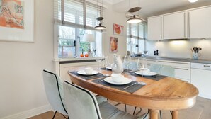 Un espace repas avec une table en bois, des chaises blanches et des luminaires suspendus.