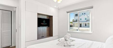 Ein Hotelzimmer mit Bett, Deckenventilator, Fernseher und Fenster mit Blick auf Gebäude.