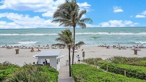 A beach with palm trees, lounge chairs, and a small building, likely a lifeguard station. - 2-Bedroom Ocean View Apartment with Kitchen in Luxury Beach Resort (Sunny Isles Beach)