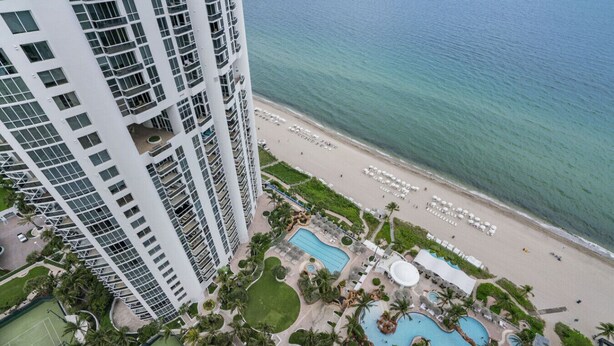 A high-rise hotel with a beach view, multiple swimming pools, and a tennis court. - 2-Bedroom Ocean View Apartment with Kitchen in Luxury Beach Resort (Sunny Isles Beach)