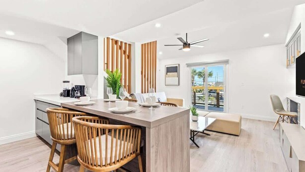 A modern kitchen with a central island, wooden chairs, and a dining area with a sofa and table. - Ocean Breeze 2C - Designer Loft & Beach Access (Panama City Beach)