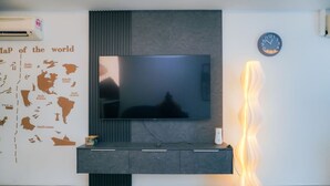 A modern living room with a flat-screen TV mounted on a dark wall, a world map on the left, and a clock on the right. - iSovo-iCity#3slep#Studio#netflix (Shah Alam)